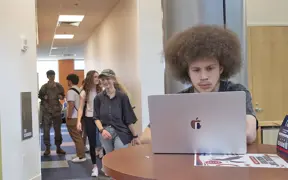 Students pass by a student doing homework on a lap top at the Business Engineering Center.