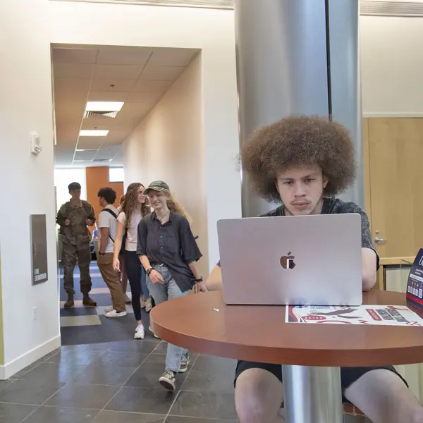 Students pass by a student doing homework on a lap top at the Business Engineering Center.
