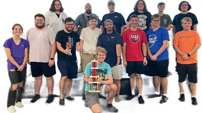 Group photo of students posing together with one person holding a trophy in front
