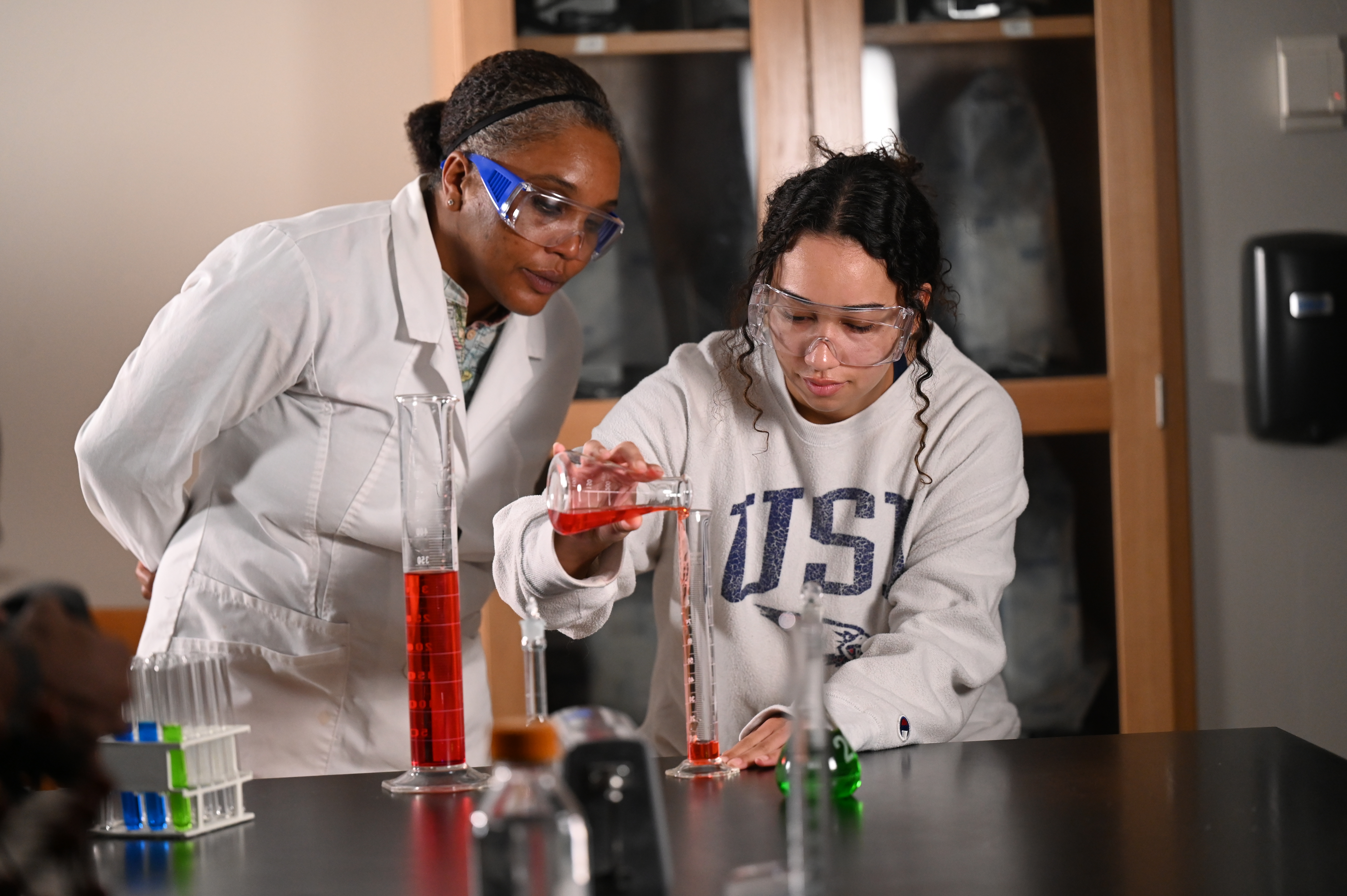 Chemistry professor and student pour chemicals into a glass beaker