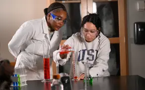 Chemistry professor and student pour chemicals into a glass beaker