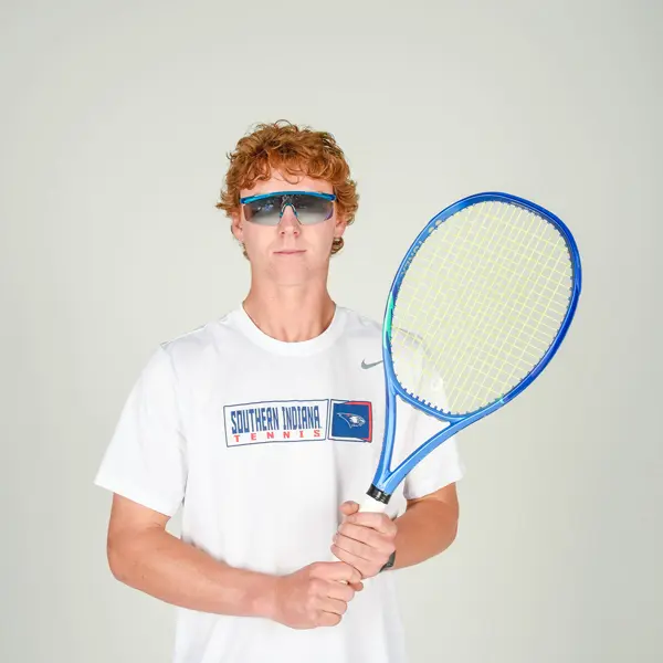A member of the tennis team, wearing sunglasses, poses with his racquet, in the studio during tennis media day.