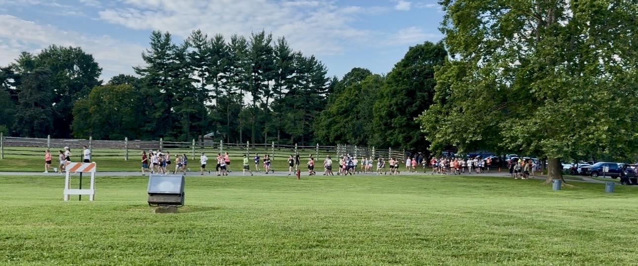 Large group of participants spread across a grassy field during a run/walk event.