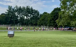 Large group of participants spread across a grassy field during a run/walk event.