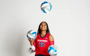 A female volleyball player juggles three volleyballs while smiling for volleyball media day.