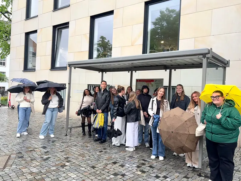 Students waiting for public transportation with umbrellas
