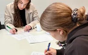 Two students seated at a table, completing an assignment