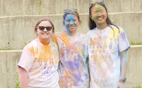 Three students covered in colorful cornflour dust smile for a photo at the Holi Festival at USI.