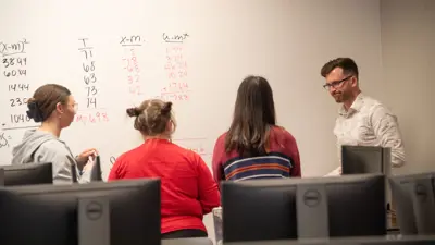 Students and faculty work at the whiteboard in a psychology research class
