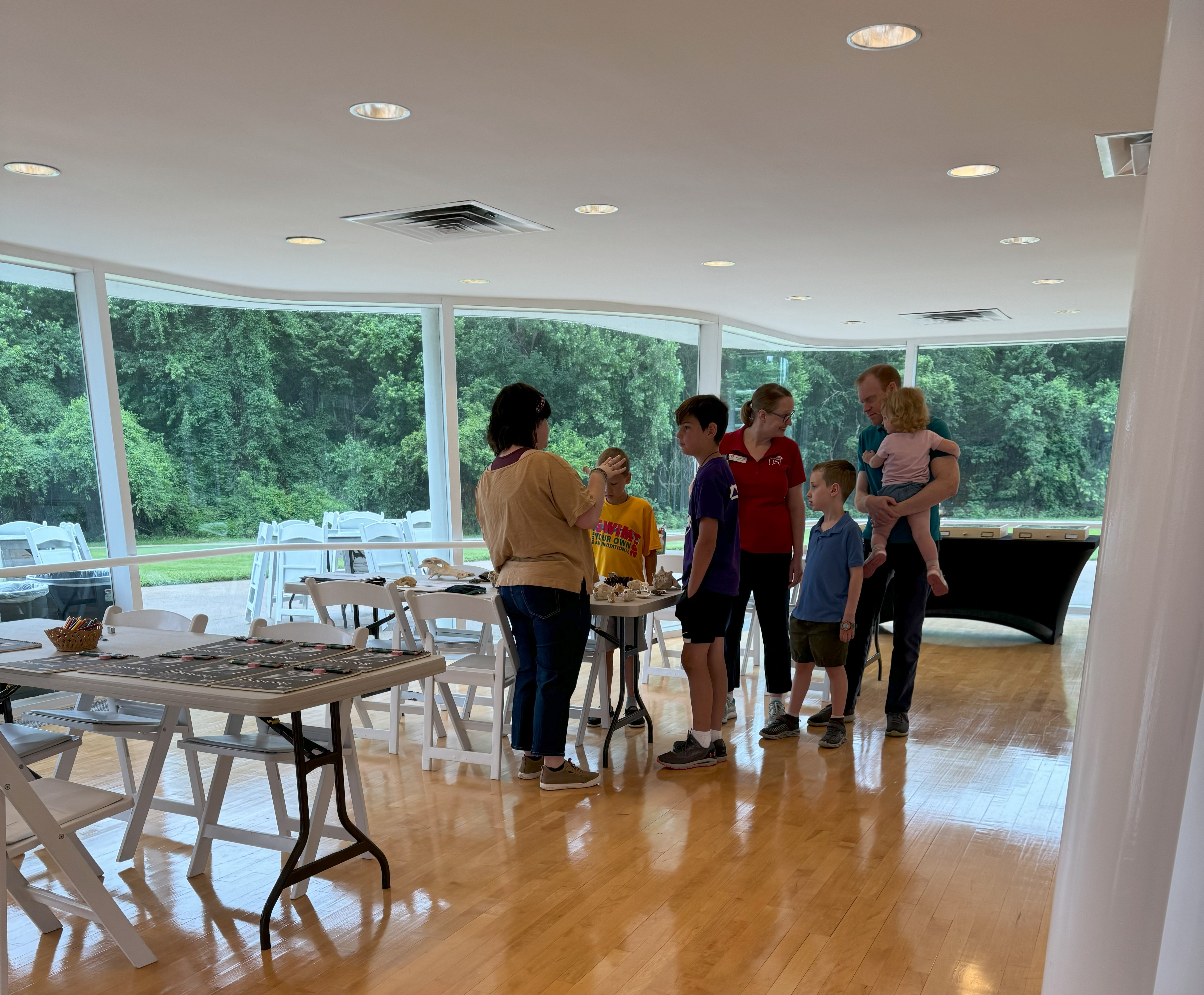 Group of people standing in a bright room with large windows overlooking greenery.