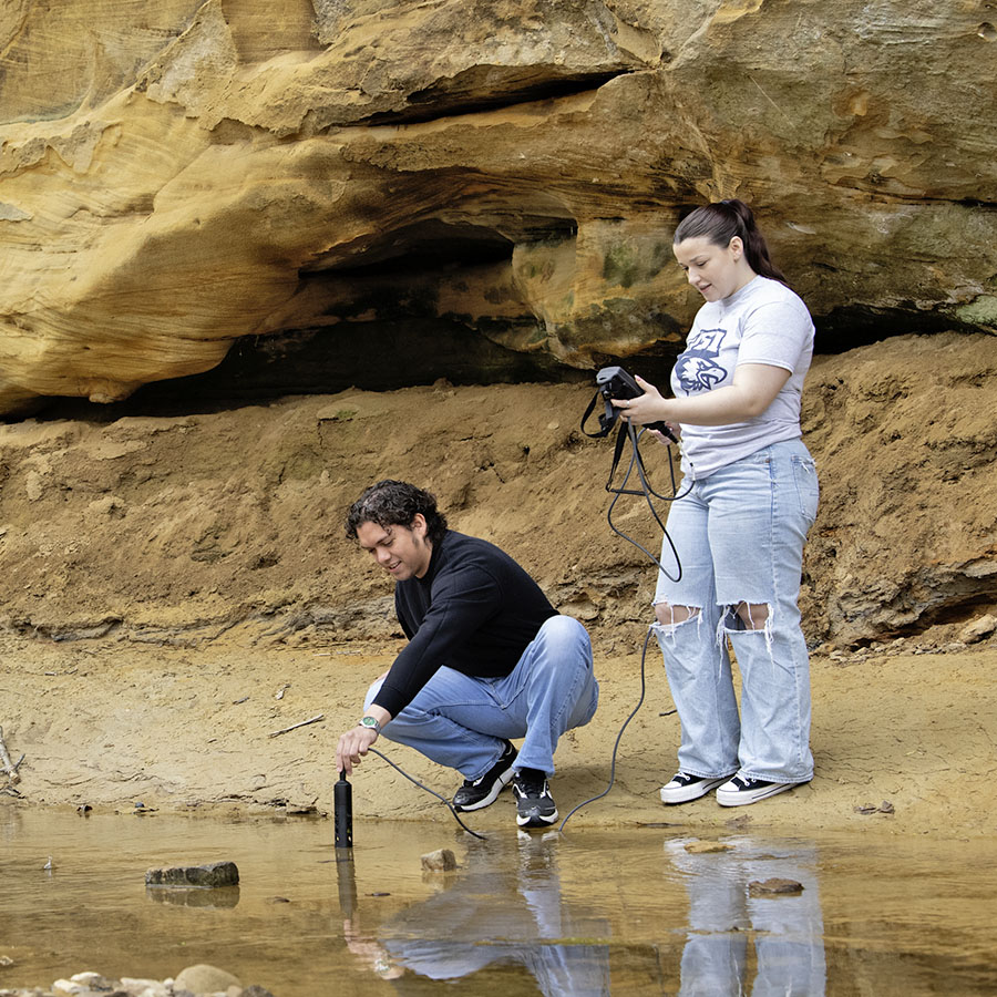 two students taking water measurements along a stream 