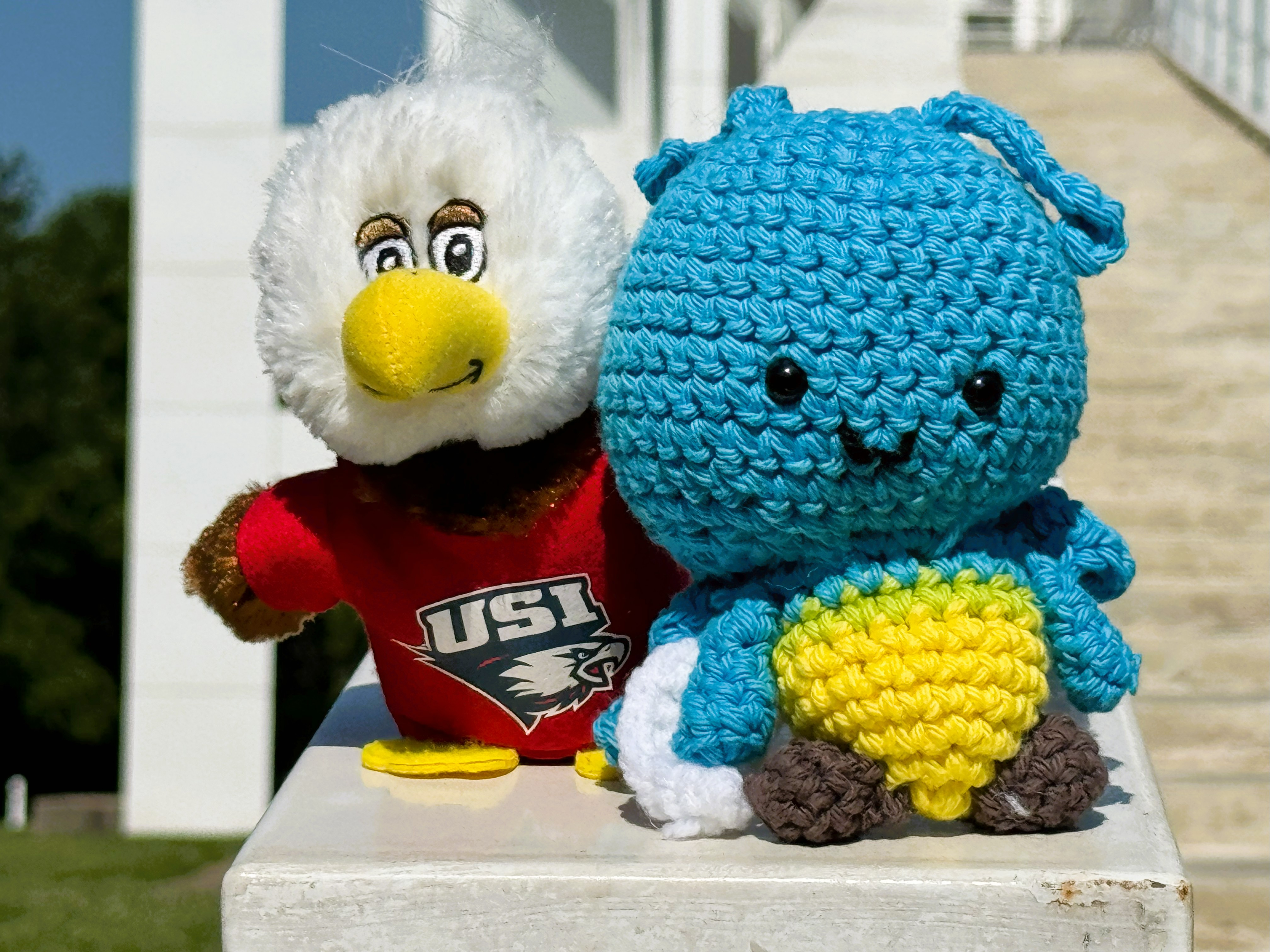 Plush blue crocheted firefly toy beside a USI eagle mascot plush wearing a red shirt.