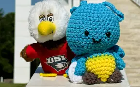 Plush blue crocheted firefly toy beside a USI eagle mascot plush wearing a red shirt.