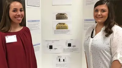 Two female students pose in front of their poster presentation at a conference