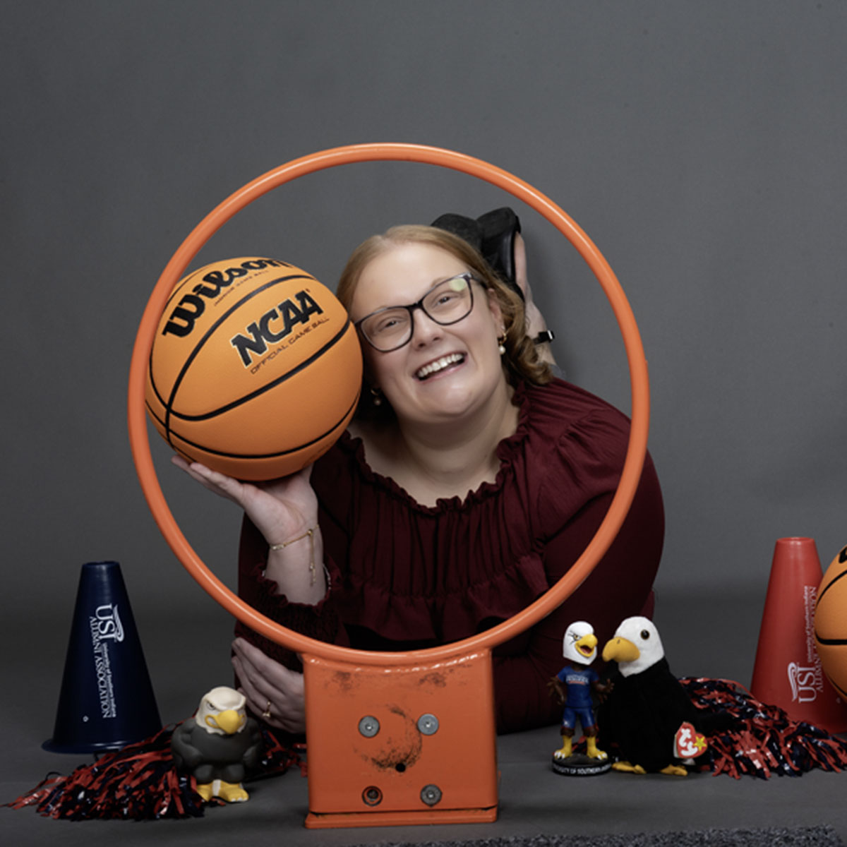 A member of the homecoming court smiles through a basketball hoop and is surrounded my little Archie Eagles, pom poms and basketball props.