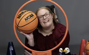 A member of the homecoming court smiles through a basketball hoop and is surrounded my little Archie Eagles, pom poms and basketball props.