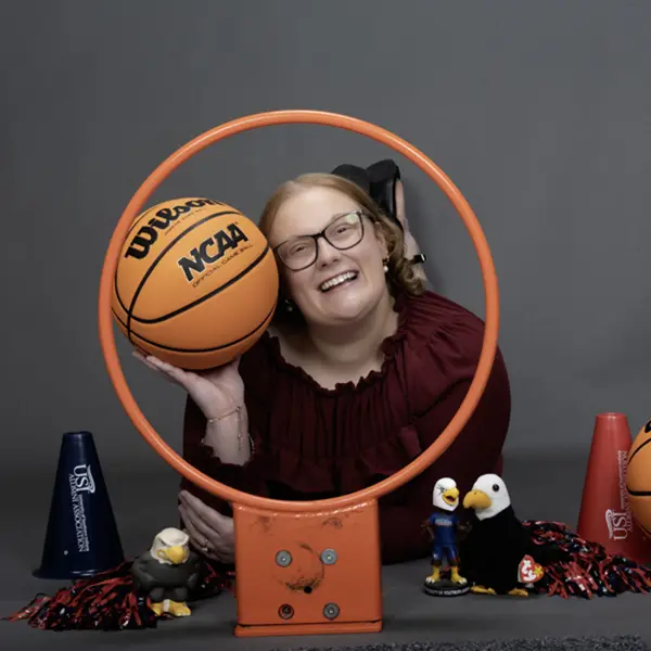 A member of the homecoming court smiles through a basketball hoop and is surrounded my little Archie Eagles, pom poms and basketball props.