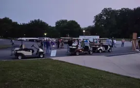 Wide view of the same area with people and golf carts arriving for the event.