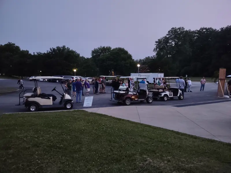 Wide view of the same area with people and golf carts arriving for the event.