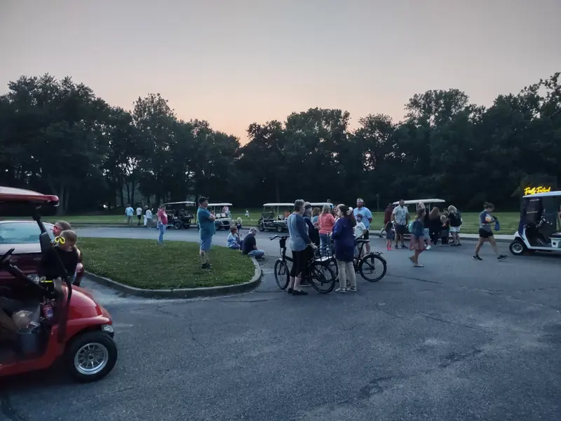 Group gathered in a circular drive area with bicycles and golf carts visible