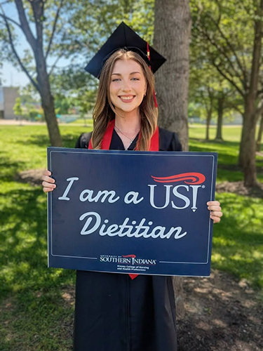 Emilie in cap and gown holding sign "I am a USI Dietitian"