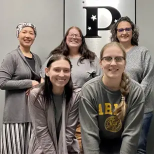 5 female USI graduates in front of Pollux Systems, INC. Logo