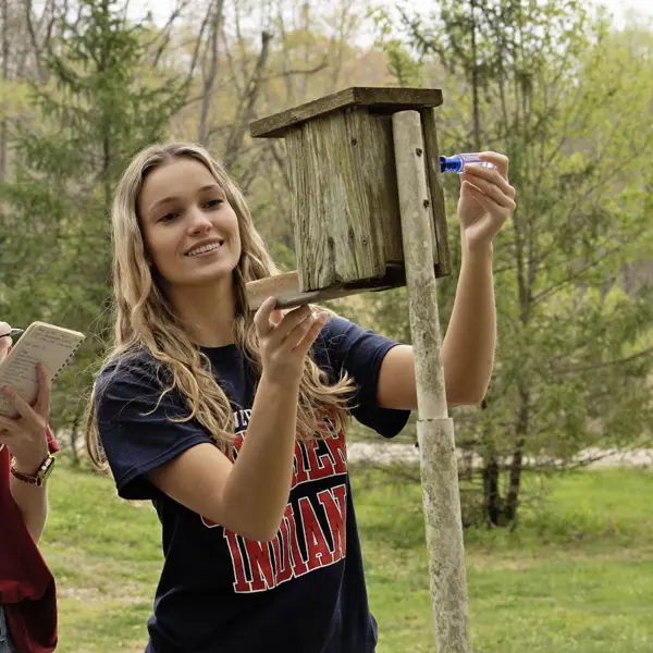 A student in orinthology class checks on a bluebird box along south eastern part of campu