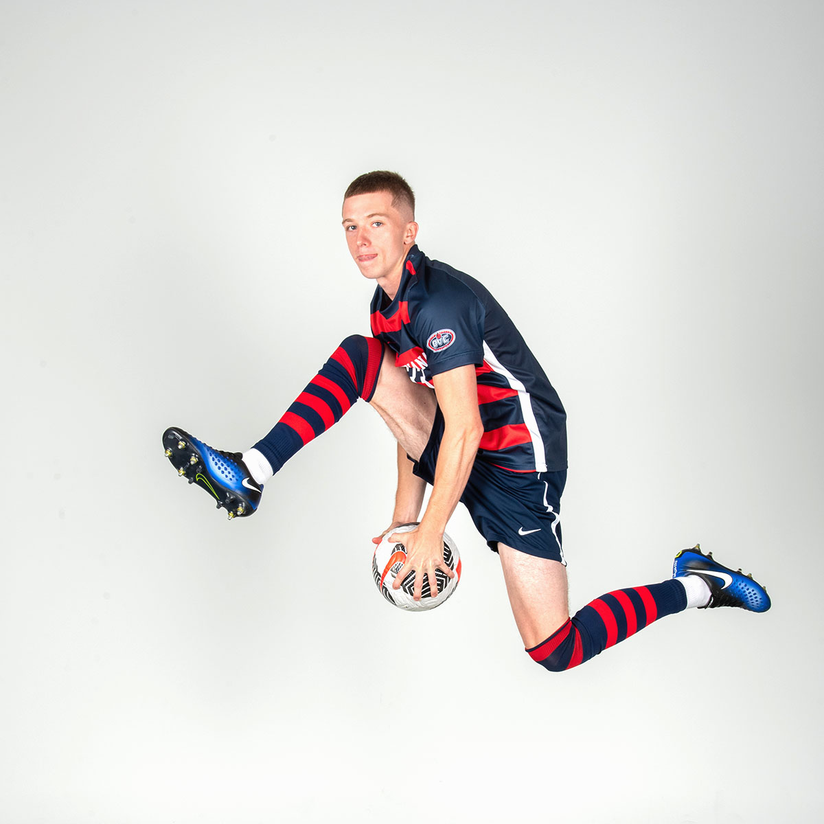 A member of soccer team jumps in the air and passes a soccer ball between his legs like he is in a slam dunk contest for media day.