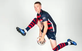 A member of soccer team jumps in the air and passes a soccer ball between his legs like he is in a slam dunk contest for media day.