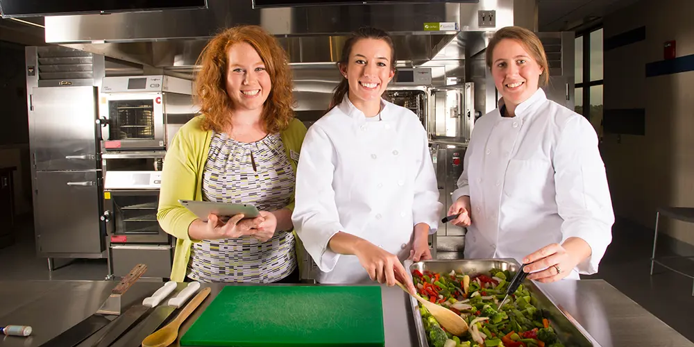 Three students smiling in the quantity food kitchen