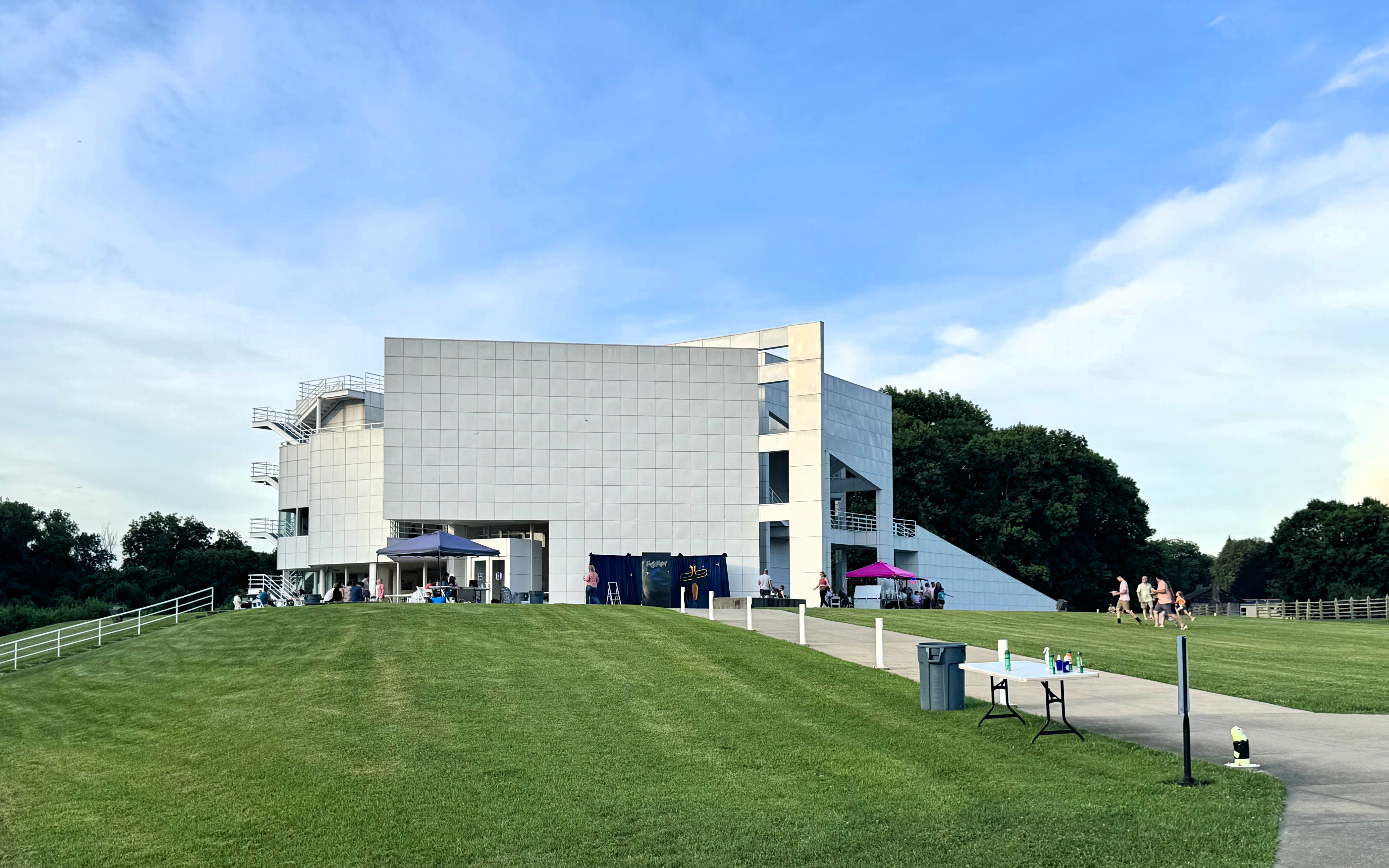 Modern white building on a grassy lawn with event setup visible outside.