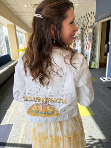 Woman wearing white jean jacket with Illuminate ALS design on back