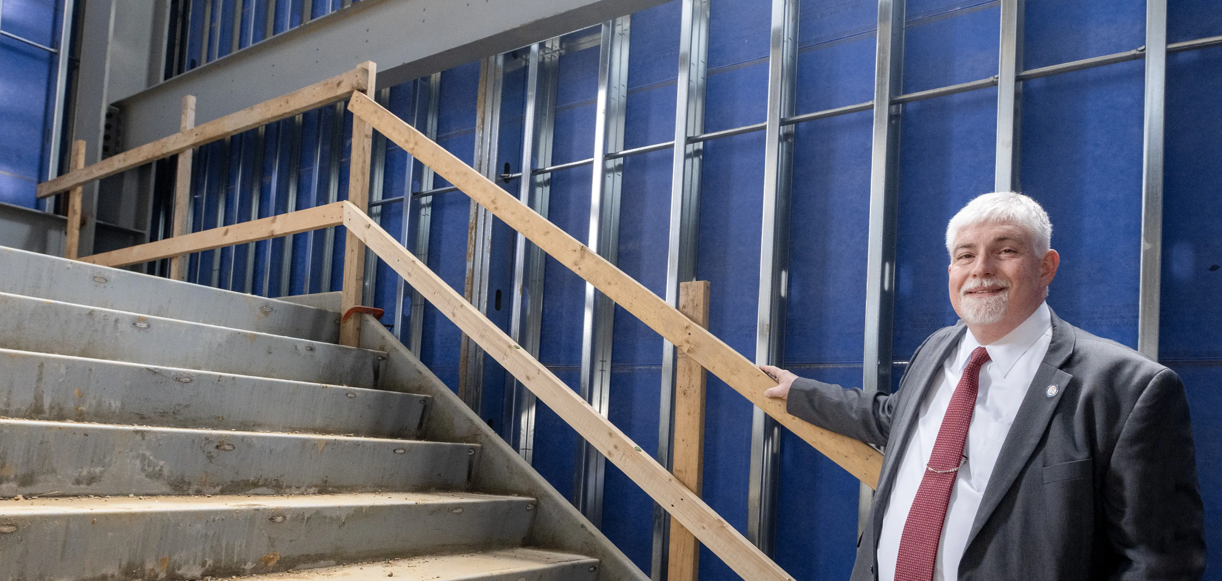 President Bridges wears a suit tie while standing on an under-construction staircase in the Health Professions Center renovation site.