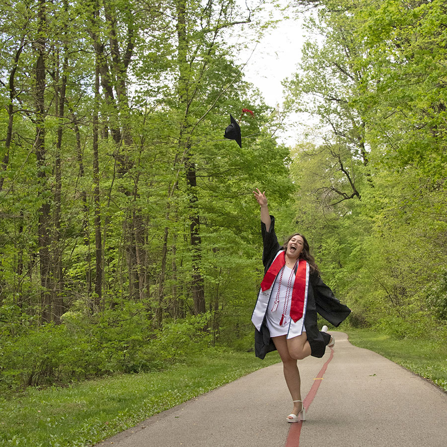 A 2025 graduate tosses her cap in the air on the USI/Burdette Trail. 