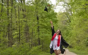 A 2025 graduate tosses her cap in the air on the USI/Burdette Trail. 