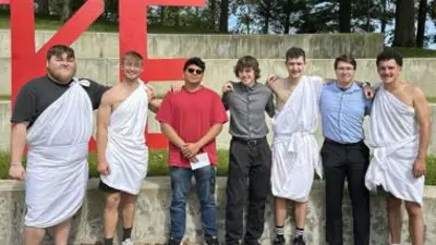 fraternity members posing for a picture with half wearing togas.