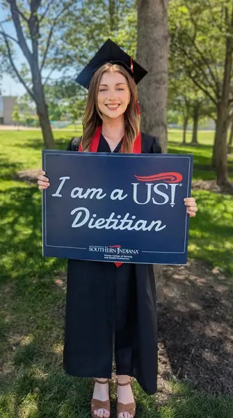 Student in cap and gown holding sign that says "I am a USI Dietitian"